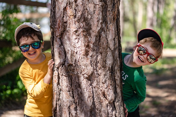 Children looking out from behind a tree with hats and sunglasses on